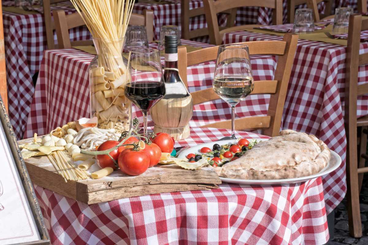 Scatto in orario dorato: tavolate vista mare sul porto di Monopoli, piatti di pesce appena serviti, pescatori e barche sullo sfondo, atmosfera conviviale e autentica